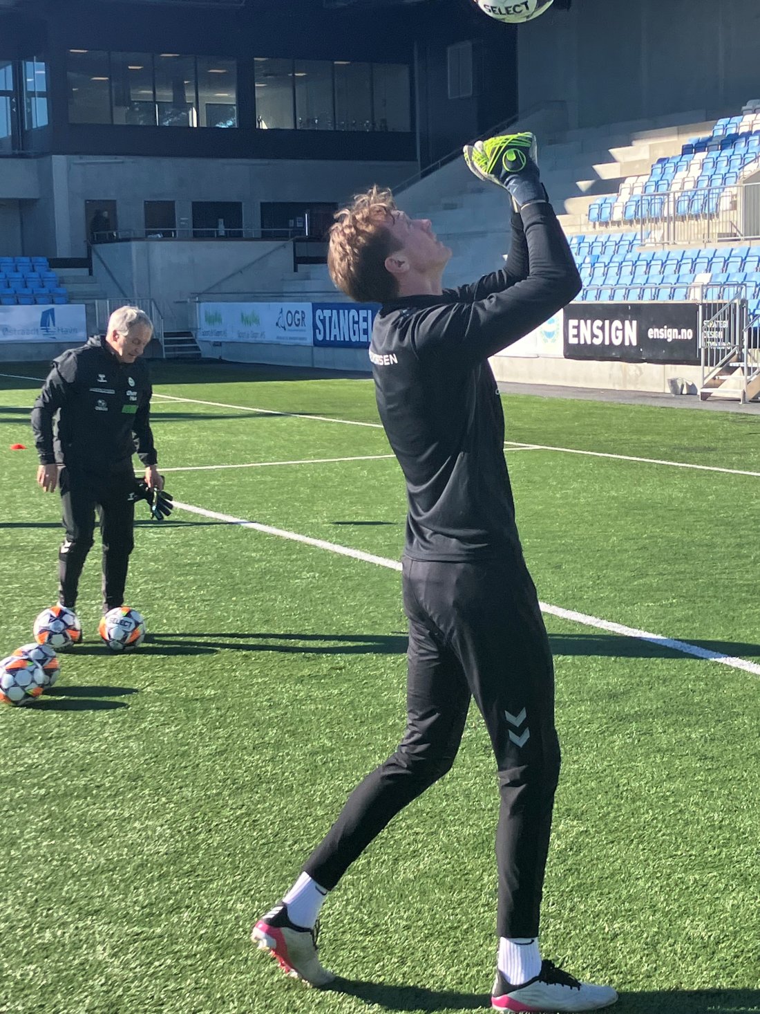 Tord Flolid bokser ballen opp i luften. Keepertrener Kjetil Østbø i bakgrunnen.
